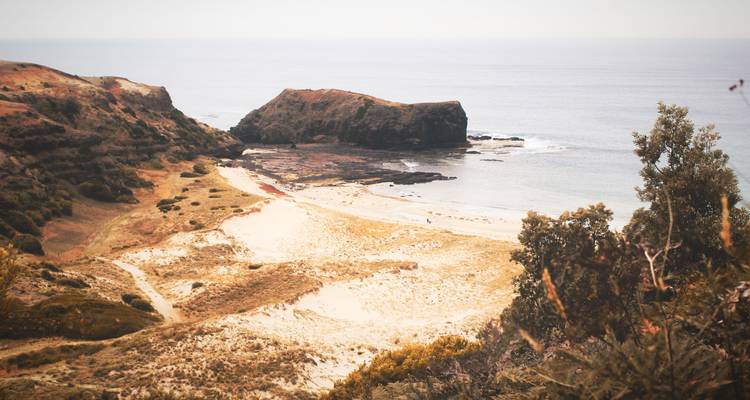 Petite crique tranquille avec des dunes de sable, des promontoires rocheux et une mer grise calme par une journée nuageuse.
