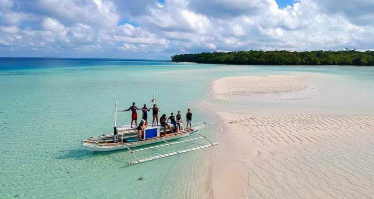 Un petit groupe se tenant sur un bateau à balancier dans une eau turquoise peu profonde à côté d'un banc de sable blanc et d'un rivage luxuriant.