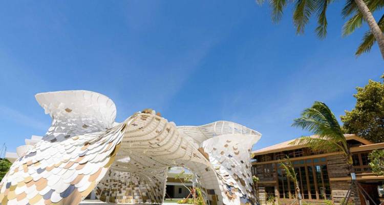 Pavillon sculptural blanc moderne aux panneaux écailleux sous un ciel bleu clair à côté de palmiers.
