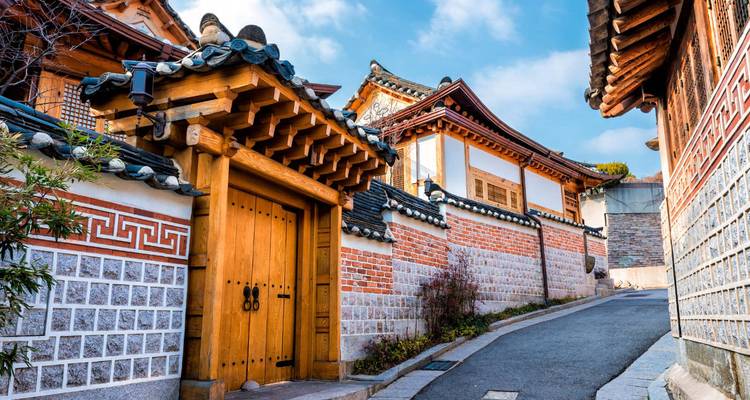 Des maisons traditionnelles coréennes hanok le long d'une ruelle étroite sous un ciel lumineux.