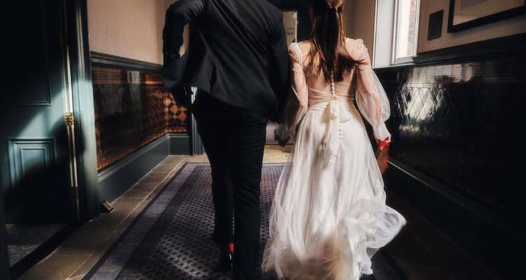 Les mariés photographiés de dos marchant dans un couloir faiblement éclairé.