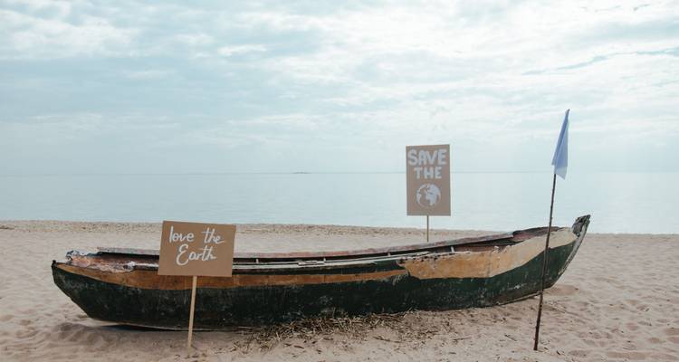 Bateau en bois usé par le temps sur une plage déserte avec des pancartes de protestation environnementale sur un fond de mer calme.