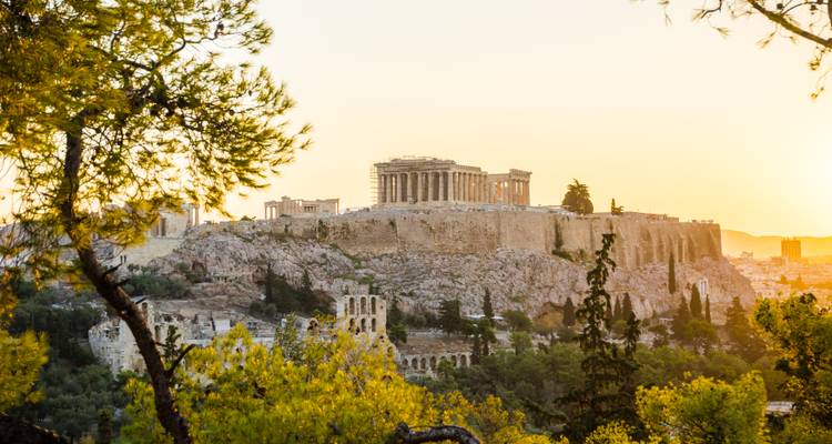 Warmes Sonnenlicht der Abenddämmerung taucht die Akropolis und die umliegenden grünen Hänge in Athen in ein weiches Licht.