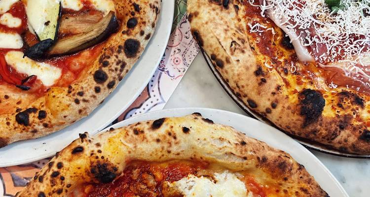 Nahaufnahme von drei neapolitanischen Pizzas, die verkohlte Krusten, frische Beläge und geschmolzenen Käse zeigen.