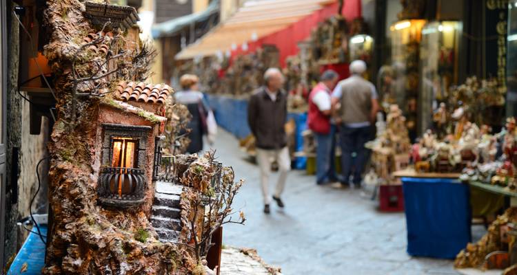 Handwerklich geprägte Gasse in Neapel mit Miniaturhäusern im Vordergrund und Besuchern, die an Ständen stöbern.