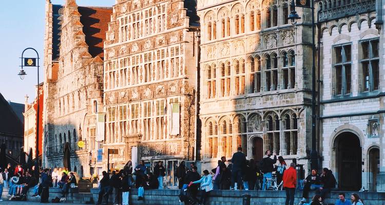 La lumière dorée du soir baigne les façades médiévales ornées et les foules le long de la rive de Gand.