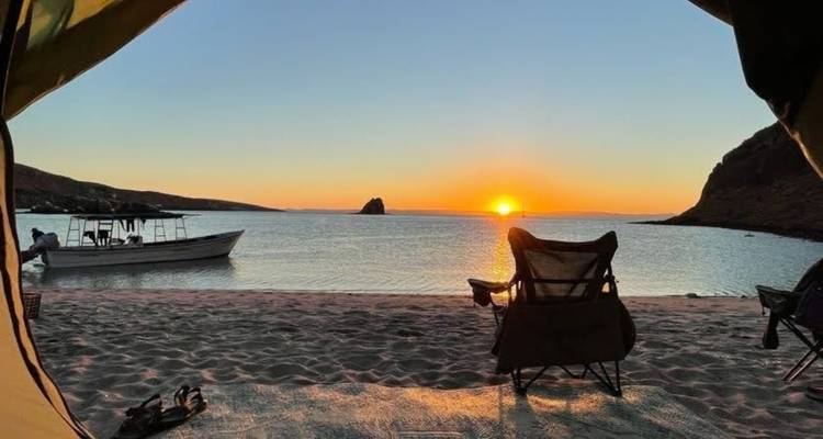 Vue depuis une tente d'une plage tranquille et d'un bateau au coucher du soleil avec des chaises sur le sable.