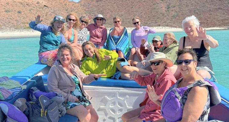 Un groupe souriant se détend sur un petit bateau au-dessus d'une eau turquoise cristalline.