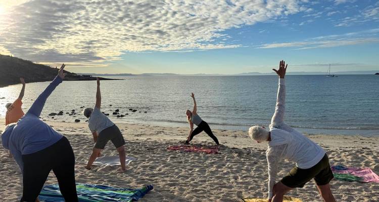 Des personnes pratiquent des étirements de yoga sur une plage de sable au lever du jour à côté des eaux calmes de la mer.