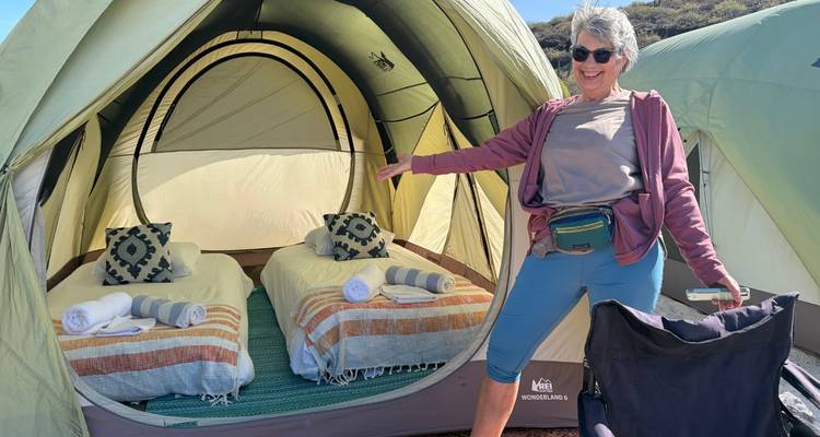 Une femme présente avec fierté l'intérieur d'une tente de glamping spacieuse avec des lits préparés.