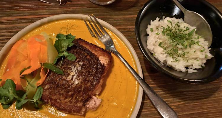 Un filet de poisson dressé avec une sauce orange éclatante et des légumes est présenté à côté d'un bol de riz.