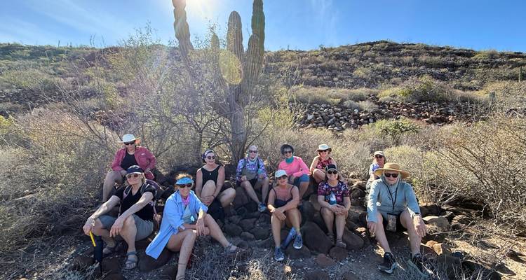 Les randonneurs se reposent à l'ombre d'un grand cactus sur une pente désertique rocheuse.