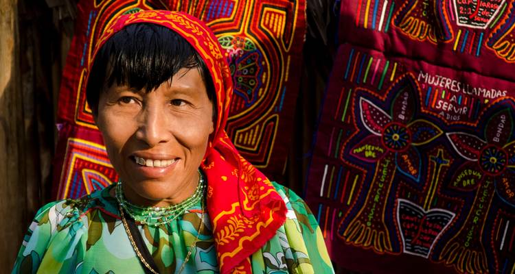 Portrait of a Kuna woman smiling, wearing a red patterned headscarf and traditional mola textiles.