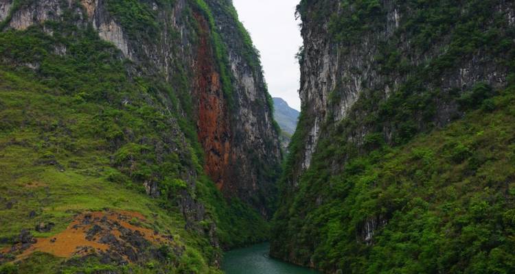 Acantilados verdes y color herrumbre que se elevan forman un desfiladero estrecho y dramático con un río sinuoso en el fondo.