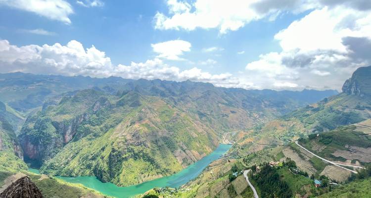 Vista panorámica a vuelo de pájaro de un sinuoso río de jade que atraviesa enormes y escarpadas cordilleras bajo nubes dispersas.