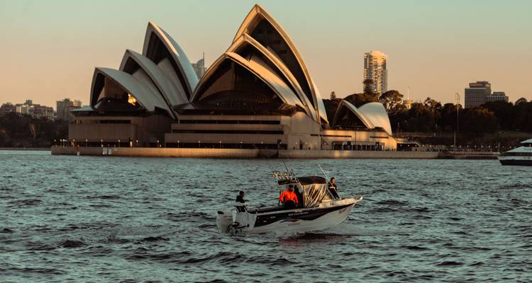 Petite vedette à moteur naviguant sur le port de Sydney avec l'Opéra House illuminée par la lumière du coucher de soleil en arrière-plan