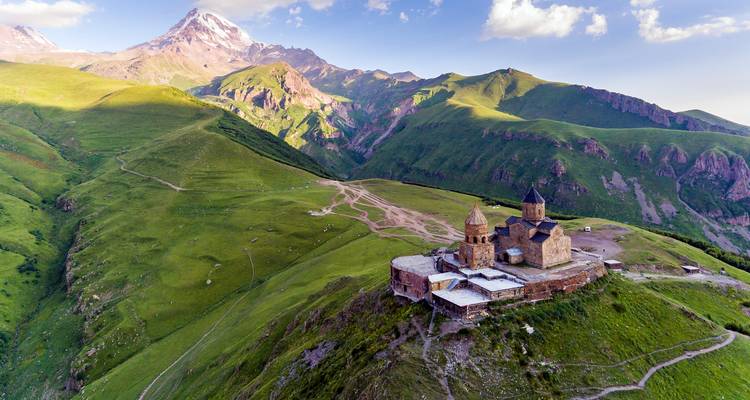 L'église de la Trinité de Gergeti, emblématique, perchée sur une crête verdoyante avec le majestueux Mont Kazbek se dressant en arrière-plan