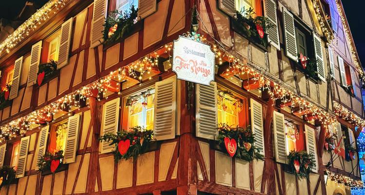 Maison à colombages étincelante de lumières festives, volets et décorationscoeur lors d'une nuit d'hiver.