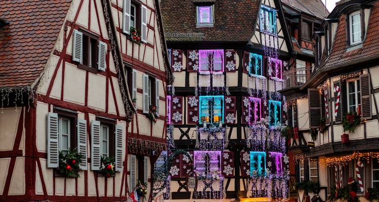 Rangée de maisons alsaciennes à colombages ornées de lumières et de décorations de Noël colorées.