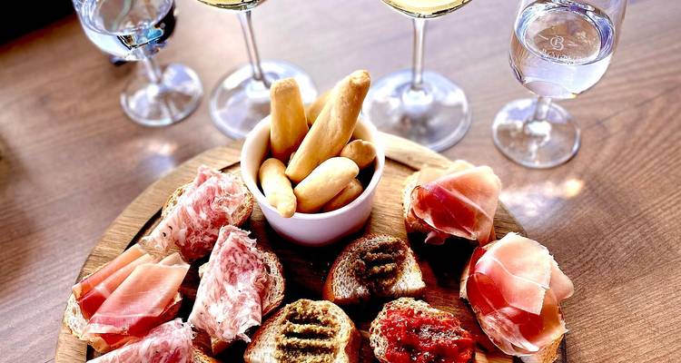 Plateau de charcuterie avec viandes froides, bruschettas et gressins accompagnés de verres de vin blanc.