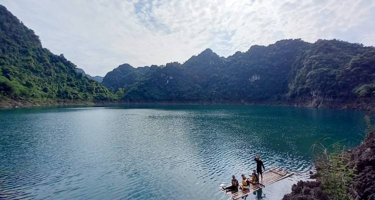 Un tranquilo lago turquesa rodeado de montañas de piedra caliza cubiertas de bosque, donde un pequeño grupo navega en una balsa de bambú.