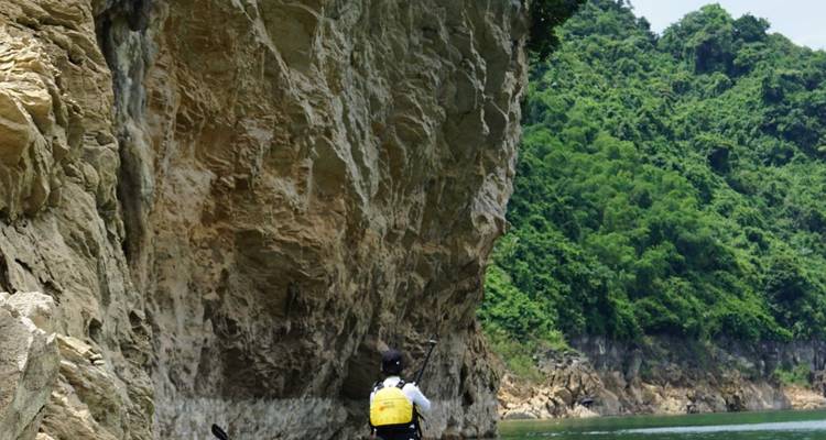 Un kayakista solitario rema bajo un acantilado de piedra caliza que se eleva majestosamente y está cubierto de vegetación.