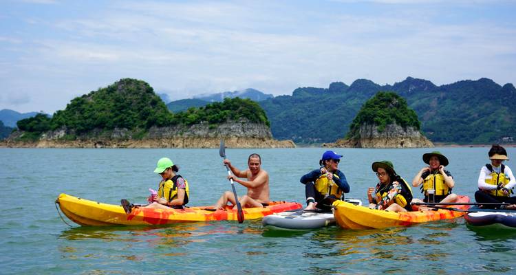Un grupo animado de remeros en kayaks brillantes y tablas de SUP en aguas esmeralda tranquilas con islotes rocosos atrás.