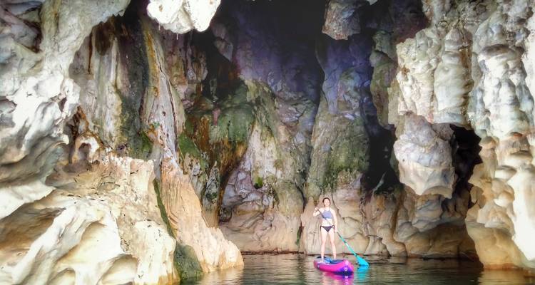 Un remero se desliza hacia una cueva dramática llena de formaciones rocosas texturizadas.