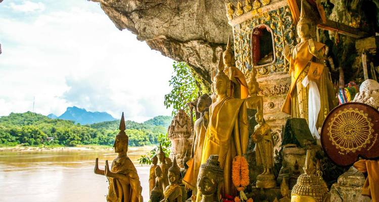 Des rangées de statues de Bouddha dorées dans la grotte de Pak Ou surplombent le fleuve Mékong et les montagnes lointaines.
