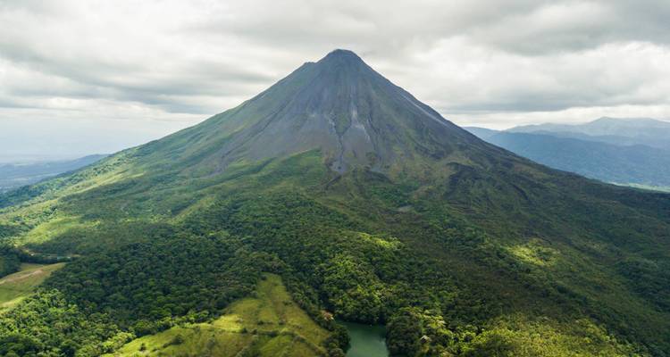 Vue aérienne spectaculaire d'un volcan parfaitement conique s'élevant au-dessus d'une forêt tropicale dense et verdoyante et d'un fleuve.