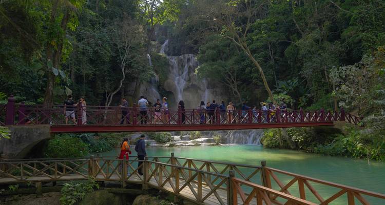 Bezoekers die op een rode brug staan voor getierde turquoise watervallen omgeven door weelderige jungle