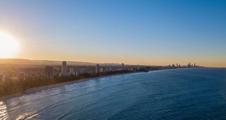 Vue aérienne du lever de soleil le long du littoral de la Gold Coast avec l'horizon urbain s'étendant jusqu'à l'horizon.