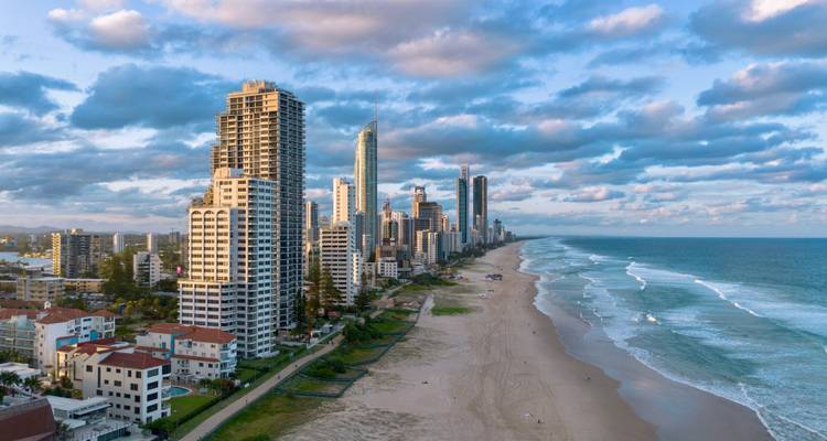 Vue aérienne des immeubles de grande hauteur de Surfers Paradise alignés le long d'une longue plage de sable fin sous des nuages épars.