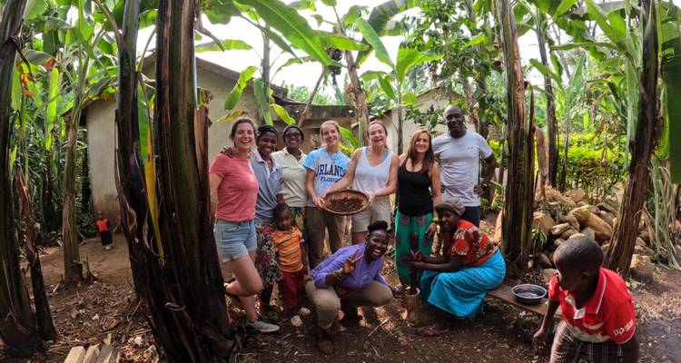 Travellers and local hosts smile among tall banana trees during a village visit, holding a woven tray.