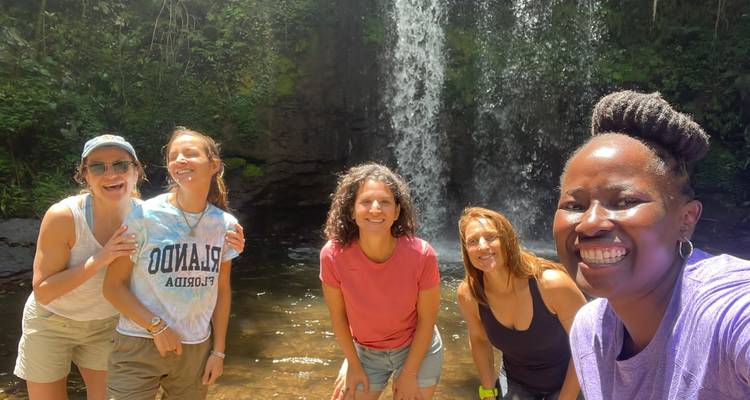 Five friends pose happily in front of a lush waterfall and pool on a sunny day.