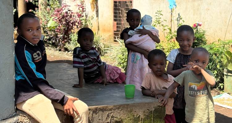 A group of local children relax and play around a concrete stoop in a village setting.