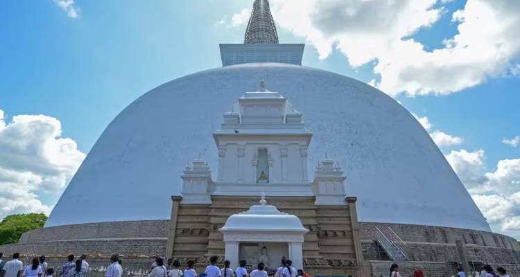 Pilger in weißer Kleidung besuchen eine riesige weiße buddhistische Stupa unter blauem Himmel.