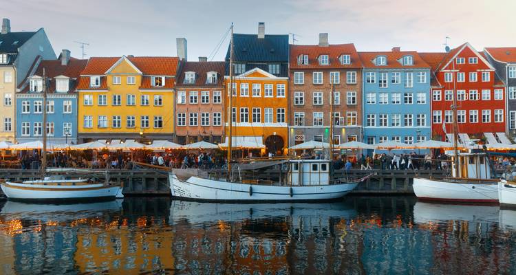 Colorful historic houses line Nyhavn canal reflected in still water at golden hour