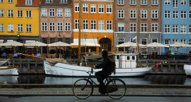 Silhouette of a cyclist passing colorful canal houses and moored boats in Nyhavn