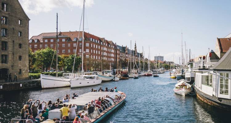 Sightseeing boat full of tourists cruising along a sunny Copenhagen canal lined with yachts