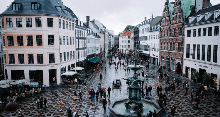 Busy pedestrian square with historic facades and central fountain on patterned pavement