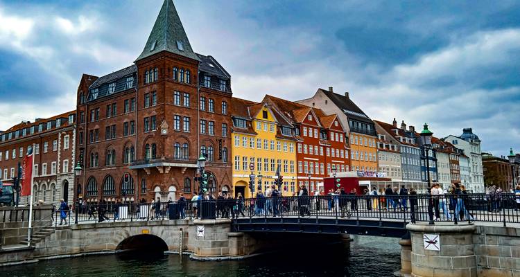 Stone bridge crosses a canal lined with historic brick and pastel buildings under cloudy skies