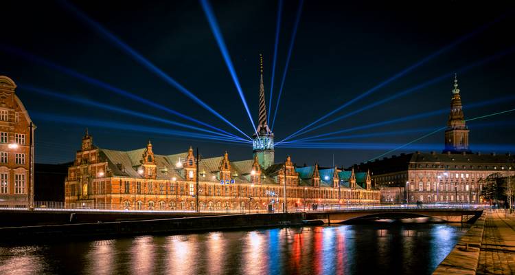Nighttime cityscape with historic building lit by vibrant blue laser beams over the canal