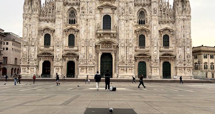 Vue de face complète de la façade de la Cathédrale de Milan avec des personnes et des pigeons sur la vaste place.