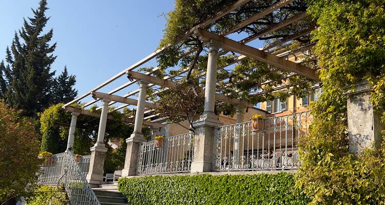 Terrasse ensoleillée avec pergola et garde-corps recouvert de lierre d'une villa au bord du lac.