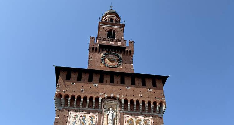 Vue ascendante de la tour de l'horloge du Castello Sforzesco contre un ciel bleu clair.