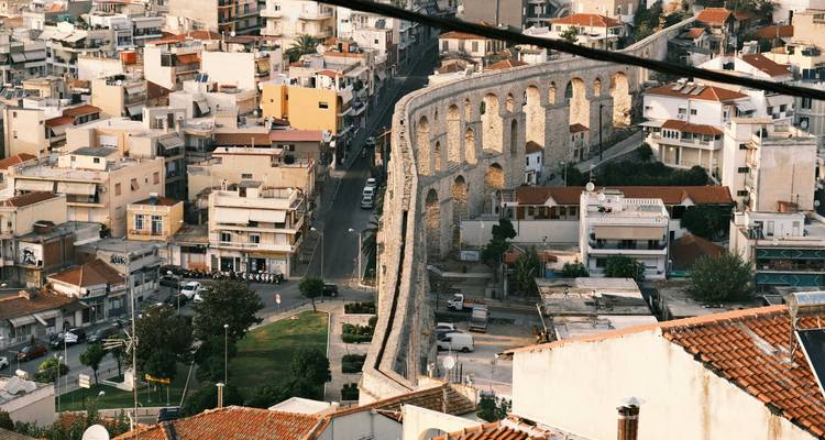 Les arches de pierre de l'ancien aqueduc de Kavala serpentent à travers le paysage urbain densément peuplé au crépuscule.