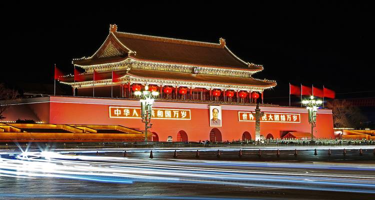 Porte de Tiananmen illuminée la nuit avec des traînées de phares de voitures au premier plan.