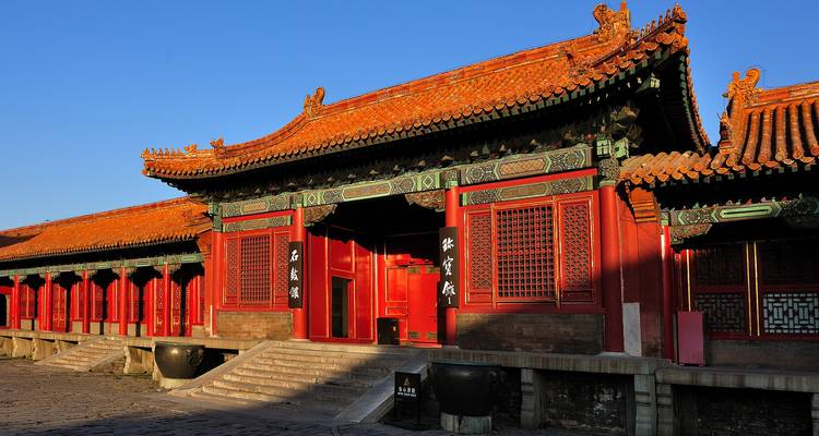 Bâtiment palatial chinois aux murs rouges traditionnels avec des avant-toits verts ornementés sous un ciel bleu dégagé.