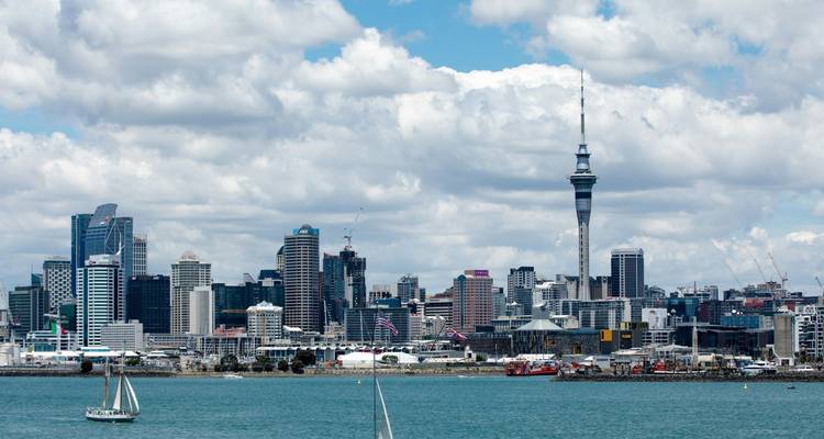Skyline moderno de Auckland con la Torre Sky elevándose sobre el puerto en un día parcialmente nublado.